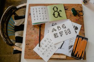 A top-down view of calligraphy tools and alphabets on a wooden table for creative lettering projects. Une vue de dessus des outils de calligraphie et des alphabets sur une table en bois pour des projets de lettrage créatifs.