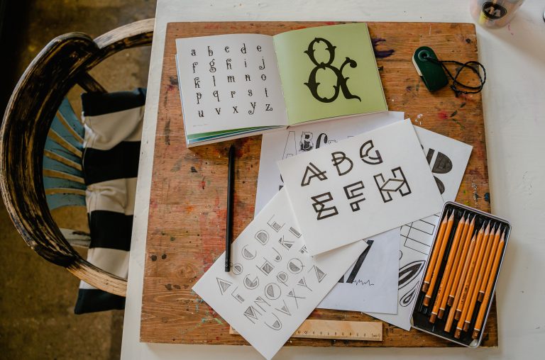 A top-down view of calligraphy tools and alphabets on a wooden table for creative lettering projects. Une vue de dessus des outils de calligraphie et des alphabets sur une table en bois pour des projets de lettrage créatifs.