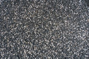 A detailed view of numerous small black chia seeds forming a textured background. Une vue détaillée de nombreuses petites graines de chia noires formant un fond texturé.