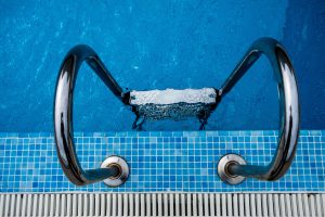 Échelle inox plongeant dans piscine bleue étincelante